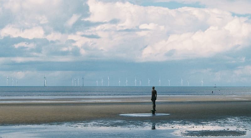 An offshore wind farm operating off the coast under a partly cloudy sky.